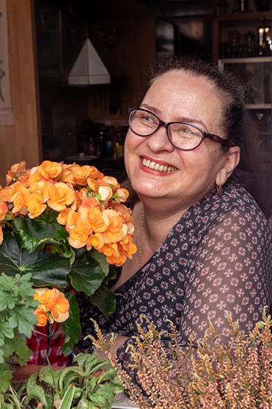 Mosolygó nő virágokkal díszített otthoni környezetben, napsütéses hangulatban.